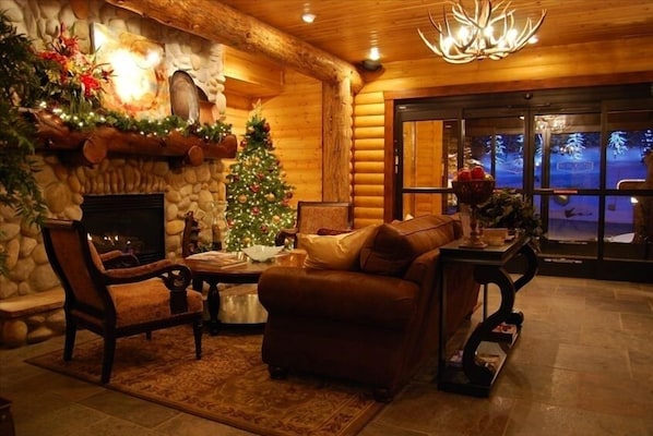 Accogliente interno di una baita in legno con camino, albero di Natale e parete in pietra.