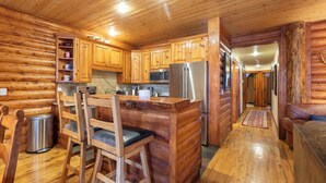 Interieur van een blokhut met houten wanden en vloeren, een keuken met een koelkast, magnetron en houten kastjes, een bar met krukken, en een woonkamer met een bank.