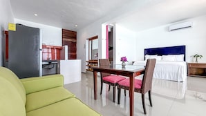 A hotel room with a bed, a dining table with chairs, a kitchen area, and a living area with a green sofa.