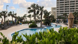 A pool area with lounge chairs, palm trees, and a large building in the background. - Royale Palms, 3rd floor,  Rare Amazing Direct Ocean Front View (Myrtle Beach)
