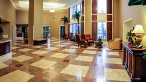 A spacious lobby with a checkered floor, seating area with chairs and a sofa, a reception desk, and large windows with shutters. - Royale Palms, 3rd floor,  Rare Amazing Direct Ocean Front View (Myrtle Beach)