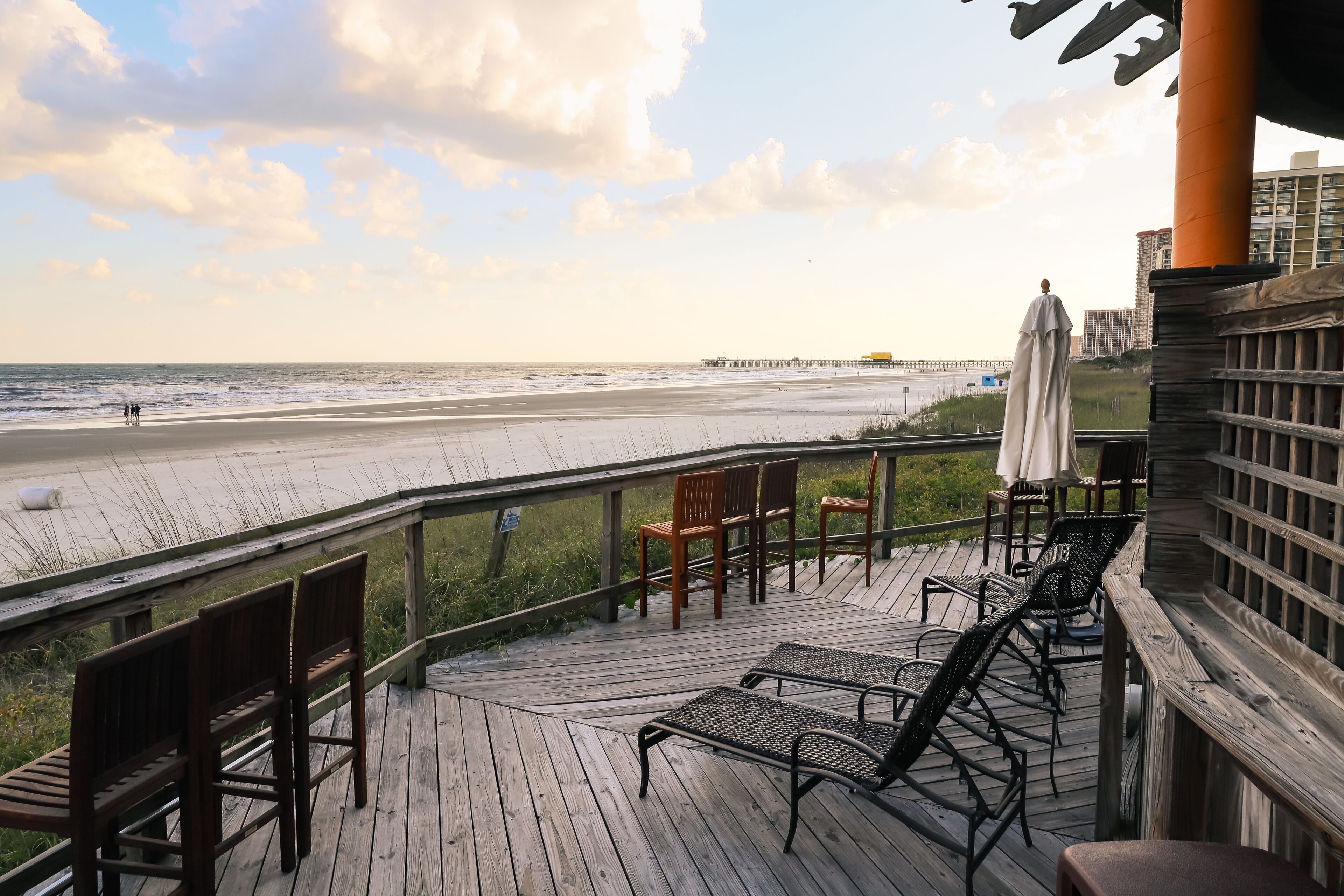 Une terrasse en bois, dotée de chaises et de parasols, qui offre une vue sur la plage.