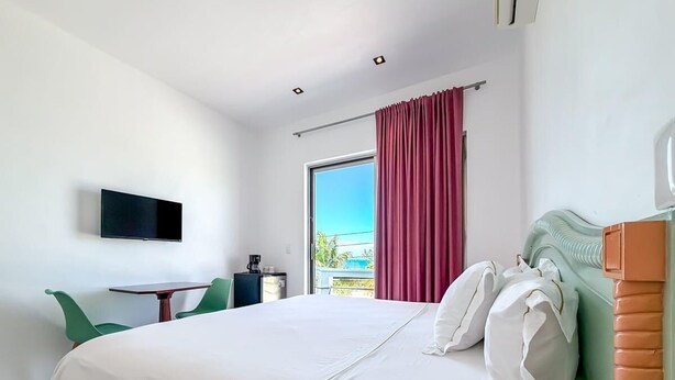 A hotel room with a bed, a desk, a chair, a TV, and a window with curtains. - 1BR with balcony (Isla Mujeres)