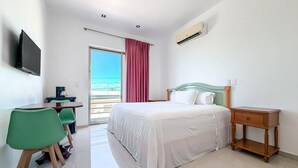 A hotel room with a bed, a desk with chairs, a TV, and an air conditioning unit. - 1BR with balcony (Isla Mujeres)