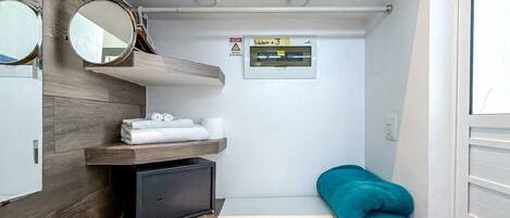 A compact bathroom with a mirror, towel rack, shelf, and a small heater.