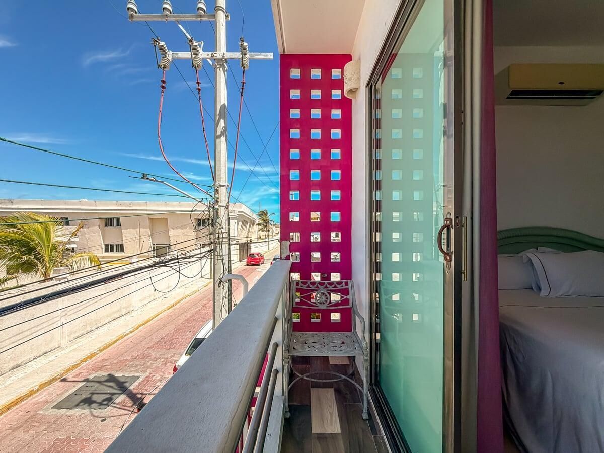Un balcone con ringhiera in metallo, un muro rosso con piccole finestre e un letto con biancheria da letto bianca.