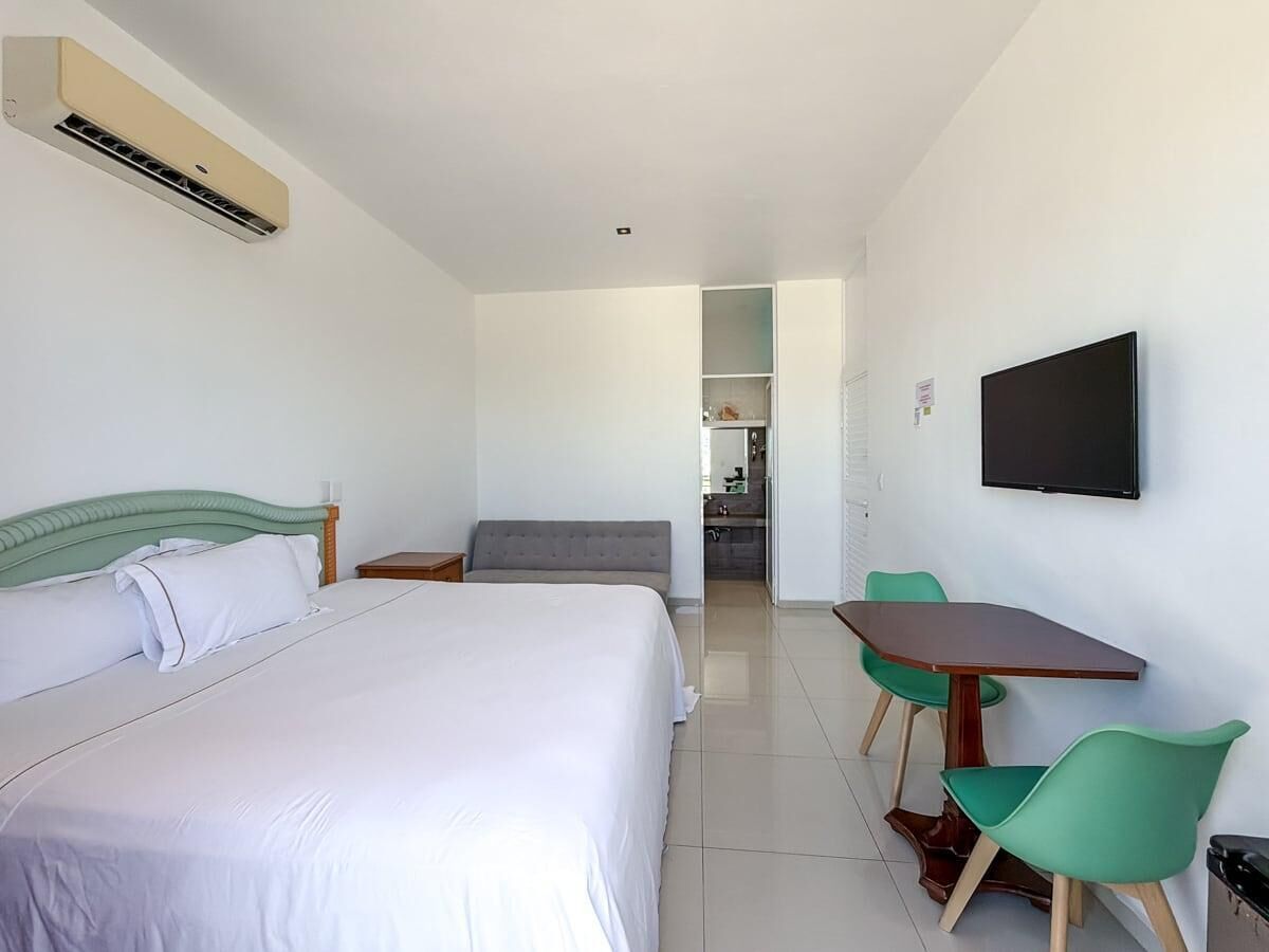 A hotel room with a bed, a desk with chairs, a television, and an air conditioning unit.