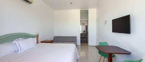 A hotel room with a bed, a desk with chairs, a television, and an air conditioning unit.