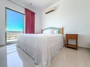 Habitación de hotel con cama, aire acondicionado, mesita de noche y vista al océano.