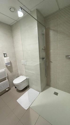 A modern bathroom with a glass-enclosed shower, a toilet, and a hand dryer.