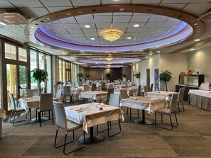 A banquet hall with multiple round tables, chairs, and a chandelier.