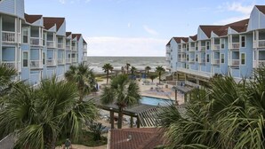 Un hotel frente a la playa con edificios de varios pisos, una piscina y palmeras.