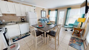Una cocina compacta con armarios blancos, una mesa de comedor con sillas, una cafetera y un refrigerador.