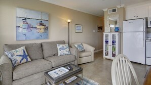 Un salon comprenant un canapé, un fauteuil, une table basse et un tableau représentant des voiliers.