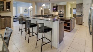 Une cuisine moderne dotée d’un grand îlot central, de tabourets de bar et d’appareils électroménagers intégrés.