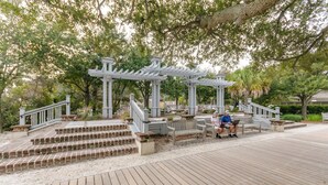 Une terrasse en bois avec une structure en forme de pergola, des marches menant à un espace détente et une personne utilisant un ordinateur portable.