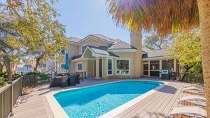 Une piscine entourée d’une terrasse en bois, avec des meubles d’extérieur et un espace patio couvert.