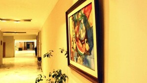 En hall med en inramad abstrakt målning på väggen, en krukväxt och en stol.
