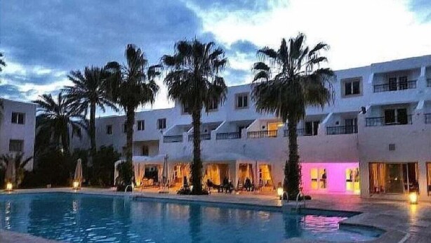 Ett hotell med en swimmingpool, palmer och en innergård.