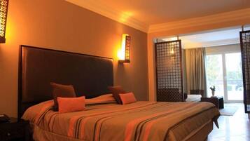 A hotel room with a large bed, a nightstand, a wall-mounted lamp, and a view of the outdoors through a sliding door.