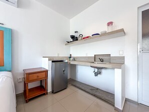 Uma cozinha compacta com frigorífico embutido, uma pequena mesa de madeira lateral e bancada com pia e estantes de arrumação.
