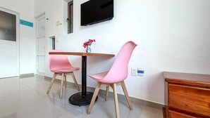 A modern room with a wooden table, two pink chairs, a round black table base, a flat-screen TV mounted on the wall, and a wooden cabinet. - Beautiful 1BR studio just steps from downtown (Isla Mujeres)