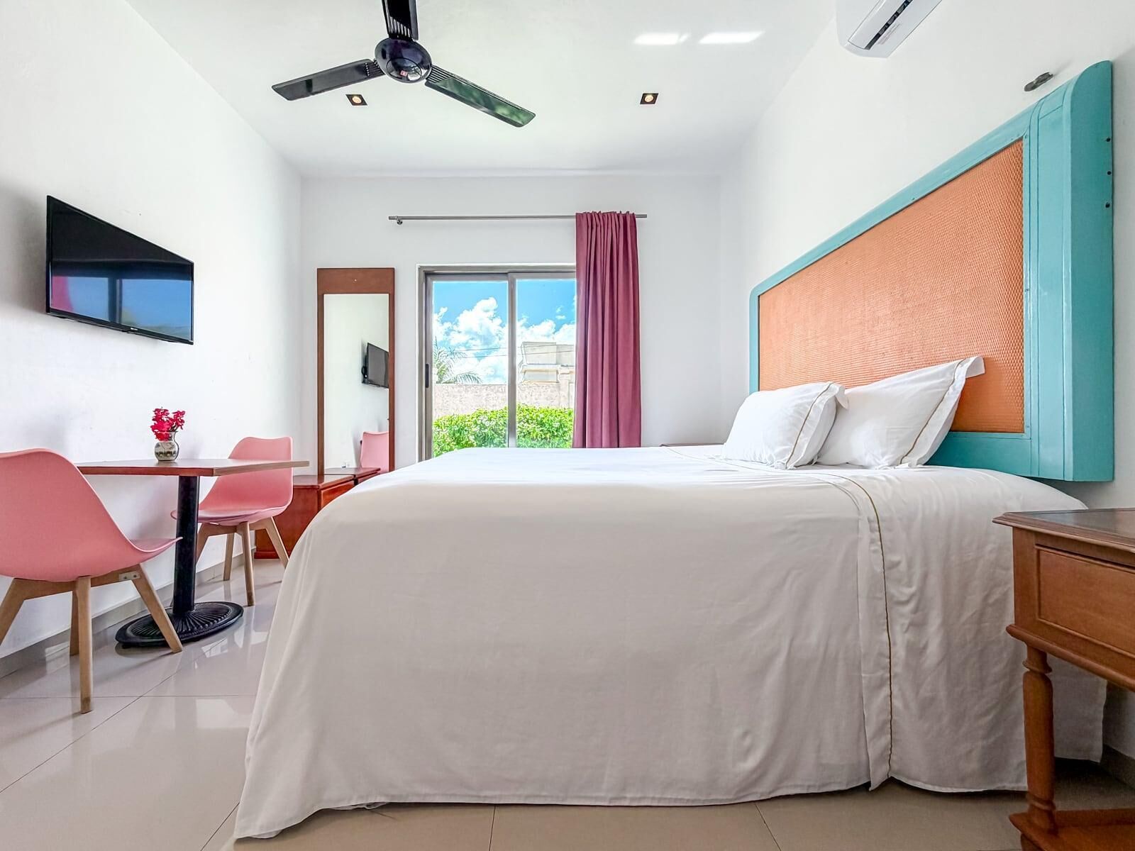Ett hotellrum med en säng, ett skrivbord, en stol, en tv och en takfläkt.