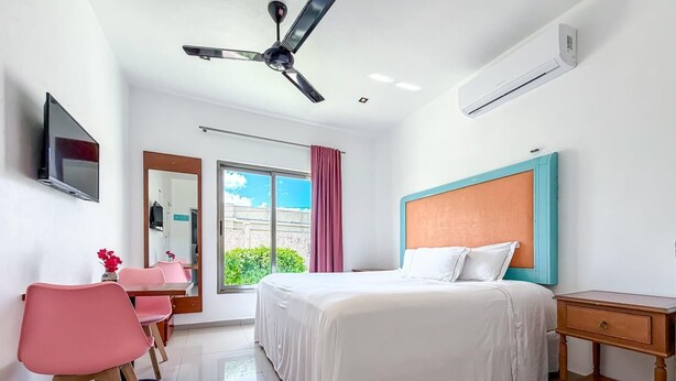 A hotel room with a bed, a desk, a chair, a television, and a ceiling fan. - Beautiful 1BR studio just steps from downtown (Isla Mujeres)