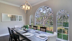 A dining room with a long table set for four, large windows with views of trees and a lake, and a chandelier above. - ☆ Tampa Riverfront Villa ☆ Heated Pool / Hot Tub / Kayaks / Pool Table (Tampa)
