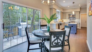 A modern kitchen with a large island, a dining area with a round table and chairs, and a view of a garden through large sliding doors. - ☆ Tampa Riverfront Villa ☆ Heated Pool / Hot Tub / Kayaks / Pool Table (Tampa)