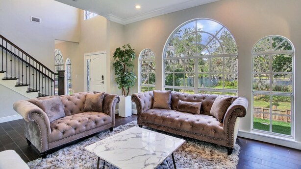 A spacious living room with two brown tufted sofas, a marble coffee table, and large arched windows offering a view of a lush garden. - ☆ Tampa Riverfront Villa ☆ Heated Pool / Hot Tub / Kayaks / Pool Table (Tampa)