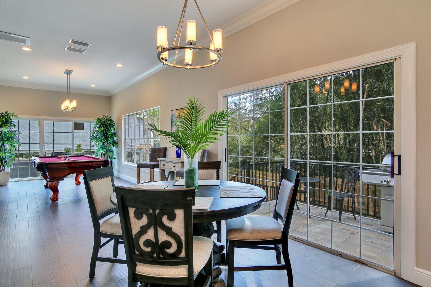 A spacious dining area with a pool table, chairs, and a large window offering a view of the outdoors.