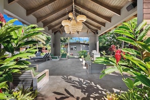 An outdoor patio area with wooden ceiling beams, hanging wicker lamps, and various seating arrangements.