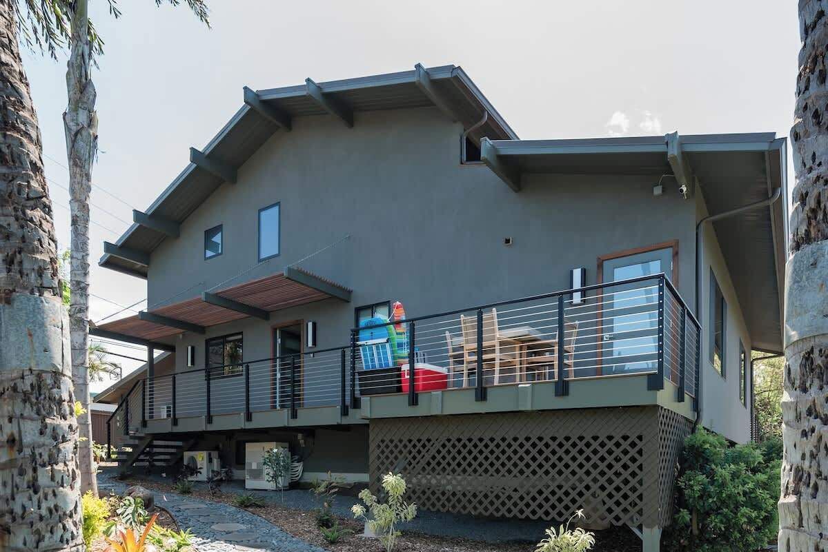 A modern two-story house with a balcony, a covered outdoor area, and a stone pillar.