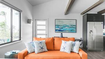 A modern living room with a sofa, a painting, and a kitchen area with a refrigerator.