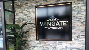 A sign for 'Wingate by Wyndham' with a stone mosaic wall behind it. - Wingate by Wyndham Long Island City (Long Island City)