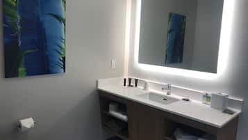 Un baño moderno con un lavamanos blanco, un espejo grande y un mueble de tocador de madera.