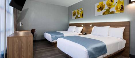 Habitación de hotel con dos camas, un escritorio, un televisor de pantalla plana y una obra de arte en la pared.