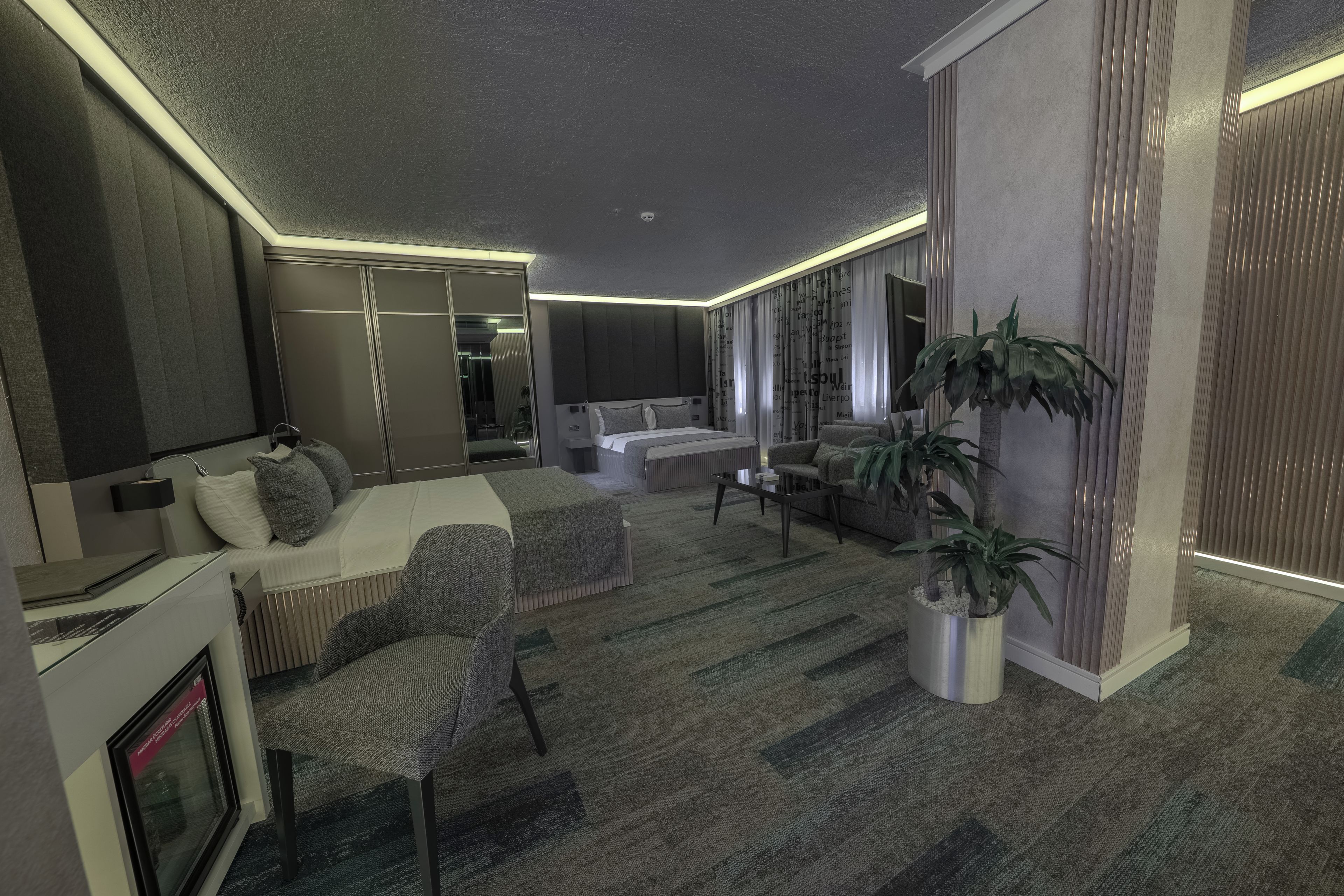 Une chambre d’hôtel moderne avec un grand lit, un coin salon comprenant un canapé et des fauteuils, une petite table et une plante en pot.