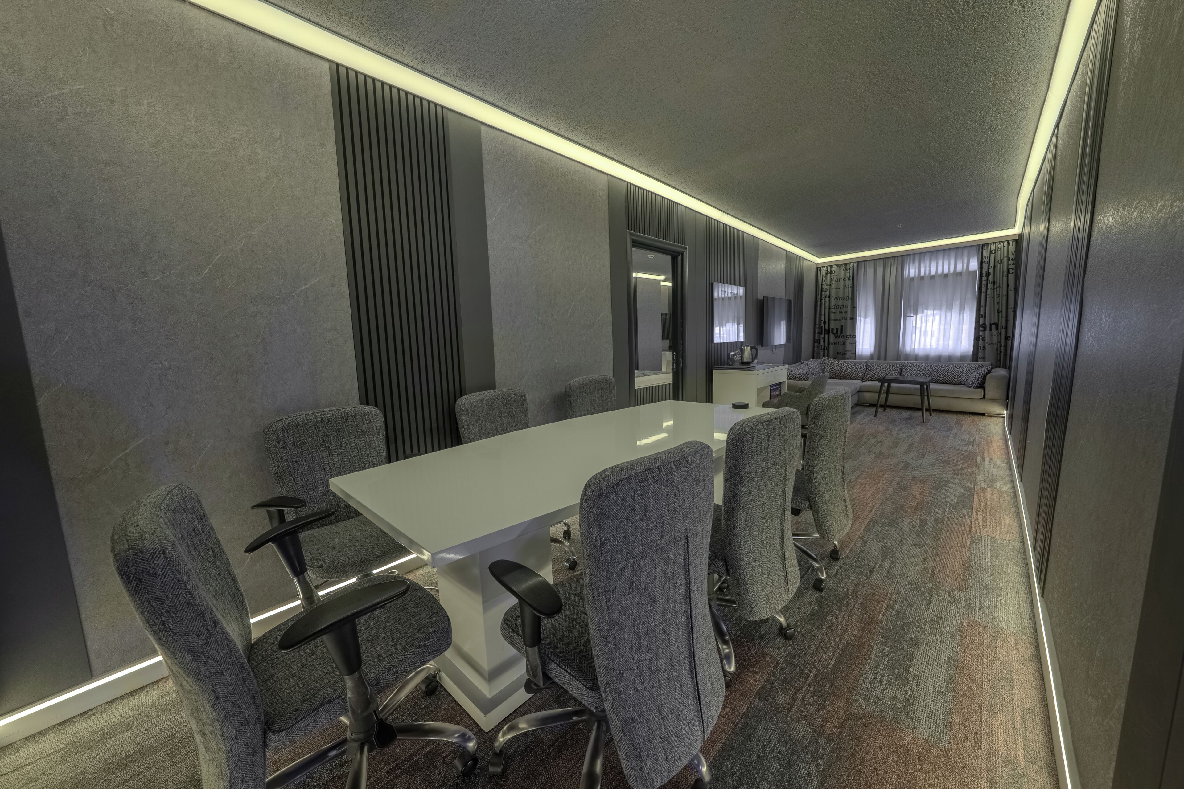 A conference room with a long table, grey upholstered chairs, and a carpeted floor.