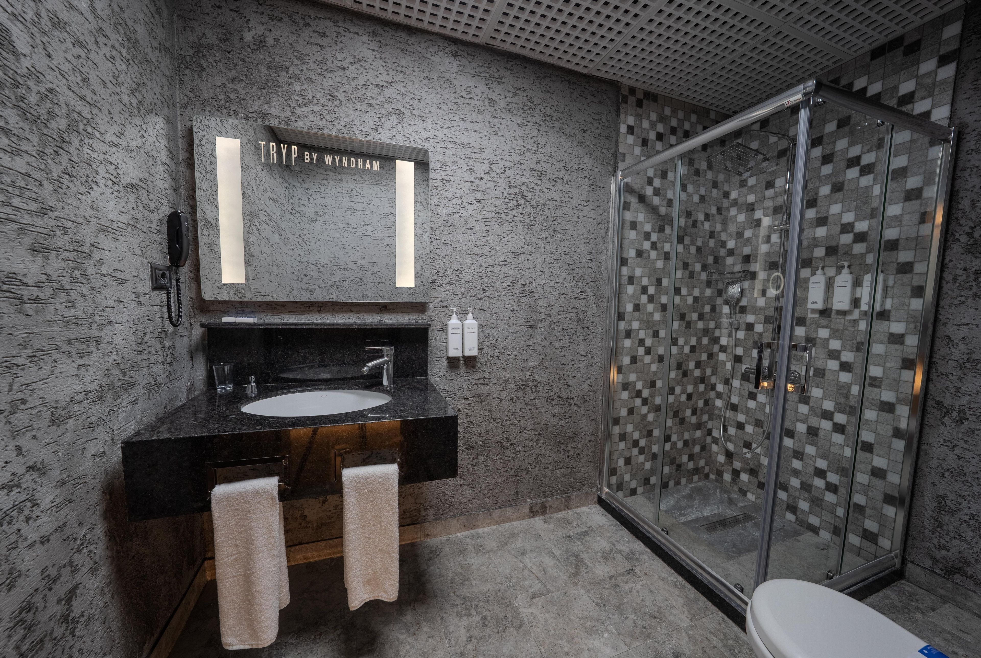 A bathroom with a granite countertop sink, a mirror, a towel rack, and a glass shower enclosure.