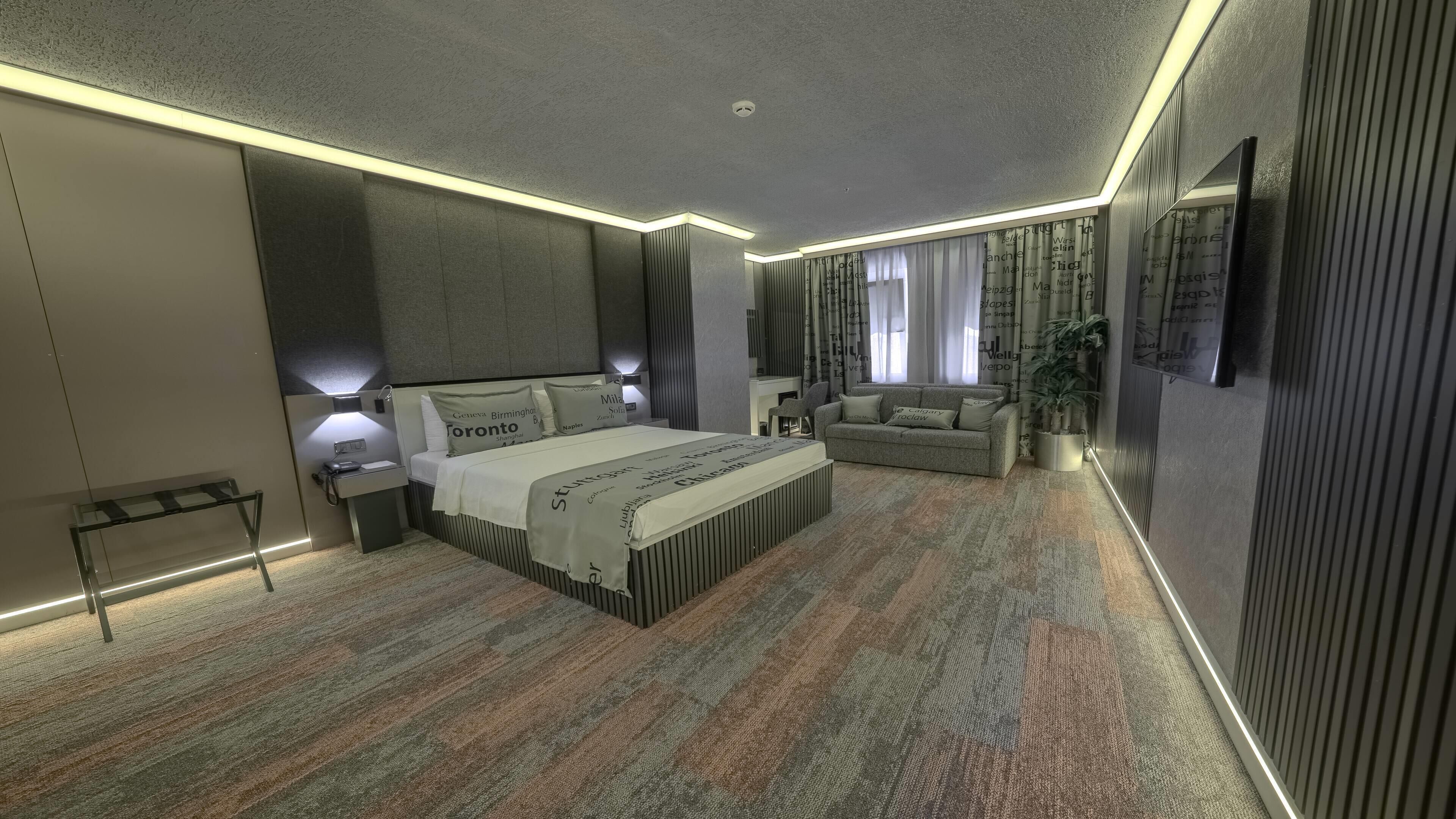 Et moderne hotelværelse med en stor seng, sengeborde, en sofa og en potteplante.