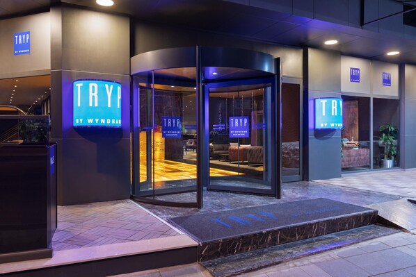 L’entrée d’un hôtel, avec une porte tournante, un comptoir d’accueil et un espace détente visible à travers les portes en verre.