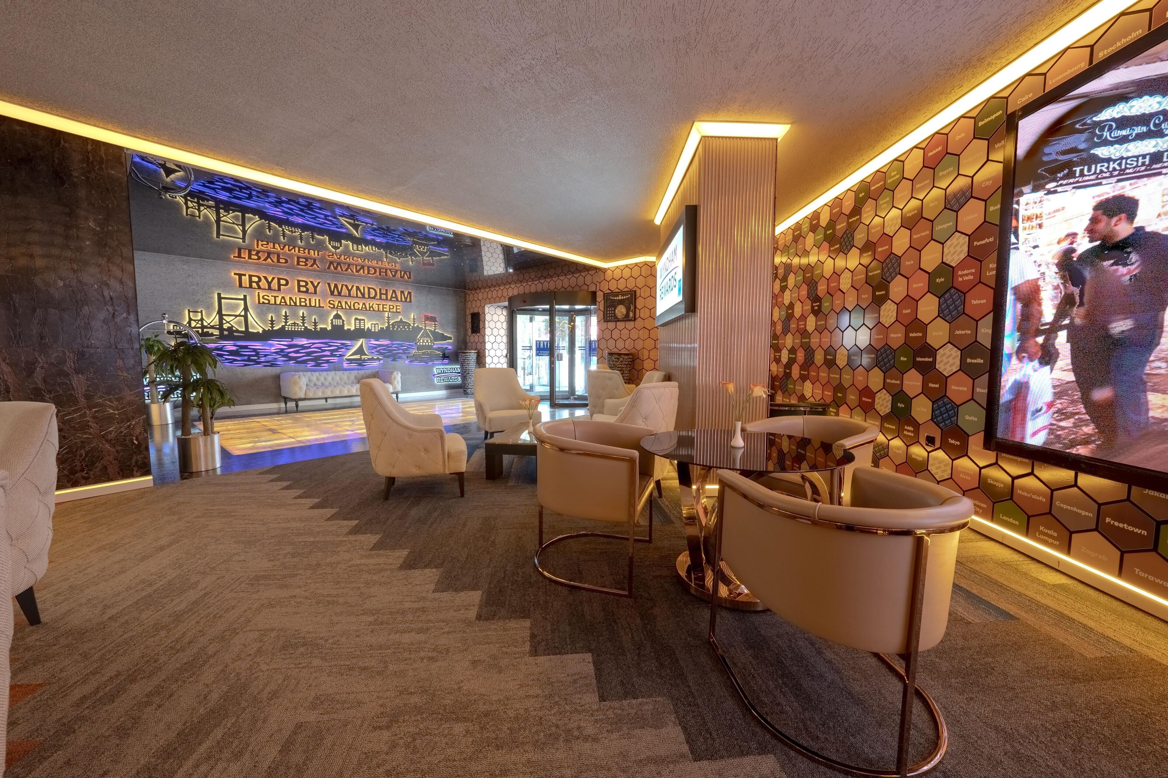 A hotel lobby with a reception desk, seating area, and a large screen displaying a person.
