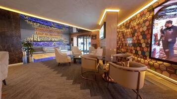 A hotel lobby with a reception desk, seating area, and a large screen displaying a person.