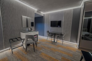 A modern hotel room with a desk, two chairs, a flat-screen TV, and a large mirror.