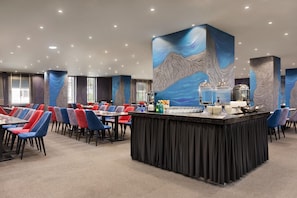 Un restaurant moderne doté d’un bar central, de plusieurs espaces de restauration et d’une grande fresque murale abstraite.