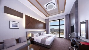 A hotel room with two beds, a sofa, a desk, a TV, and a large window with a view. - Ramada Hotel & Suites by Wyndham Gangwon Pyeongchang (Pyeongchang)