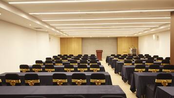Un salón de conferencias con filas de mesas y sillas, un atril y un escritorio para el orador.