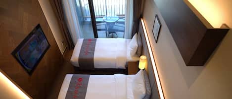 A hotel room with two beds, a small table, a wall-mounted TV, and a balcony with a table and chairs.